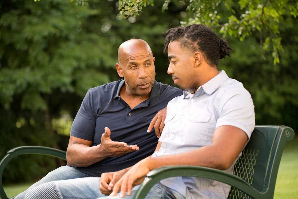 A young man being mentored by an older gentleman at a park bench.