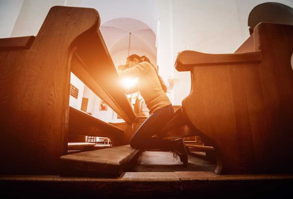 A woman kneeling at a church, praying to God.
